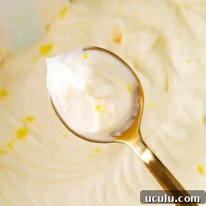 Holding up a spoon of lemon cream cheese frosting to show thick and fluffy texture