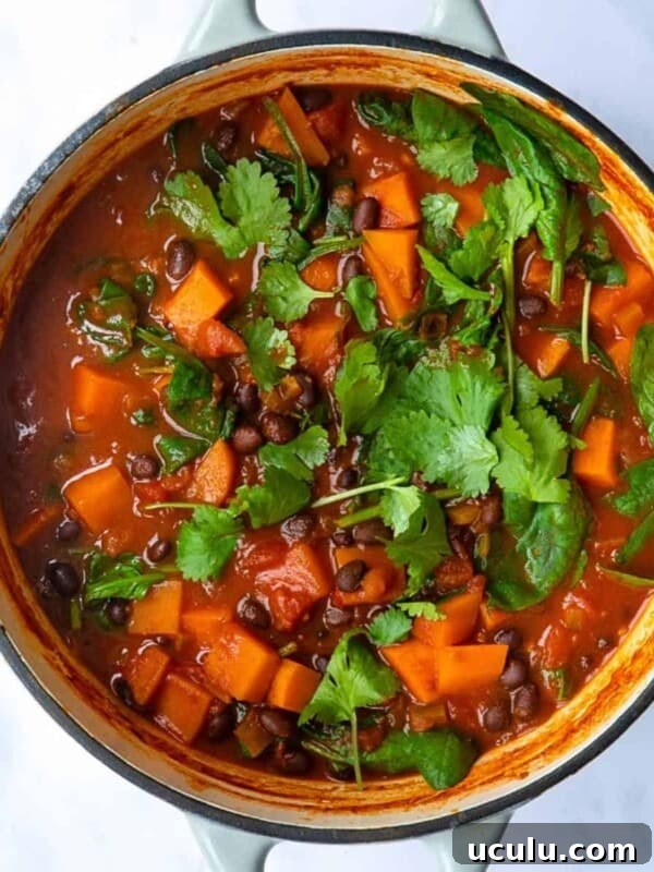 Sweet Potato and Black Bean Stew served in a large pot topped with coriander. The pot is displayed on a white marble background.