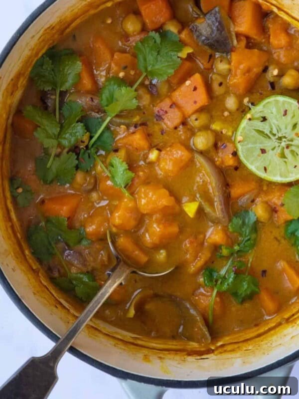Sweet Potato Satay Curry served in a large pot with a metal spoon on a white marble background