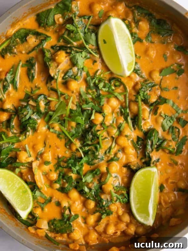 chickpea curry topped with fresh lime wedges and freshly chopped coriander in large pan.