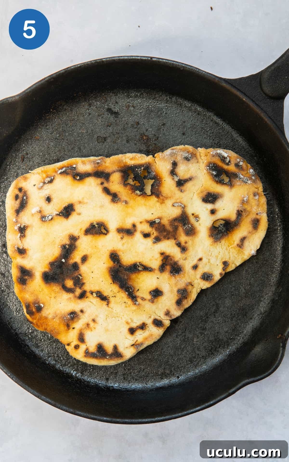 gluten free naan bread being dry fried in large black frying pan.