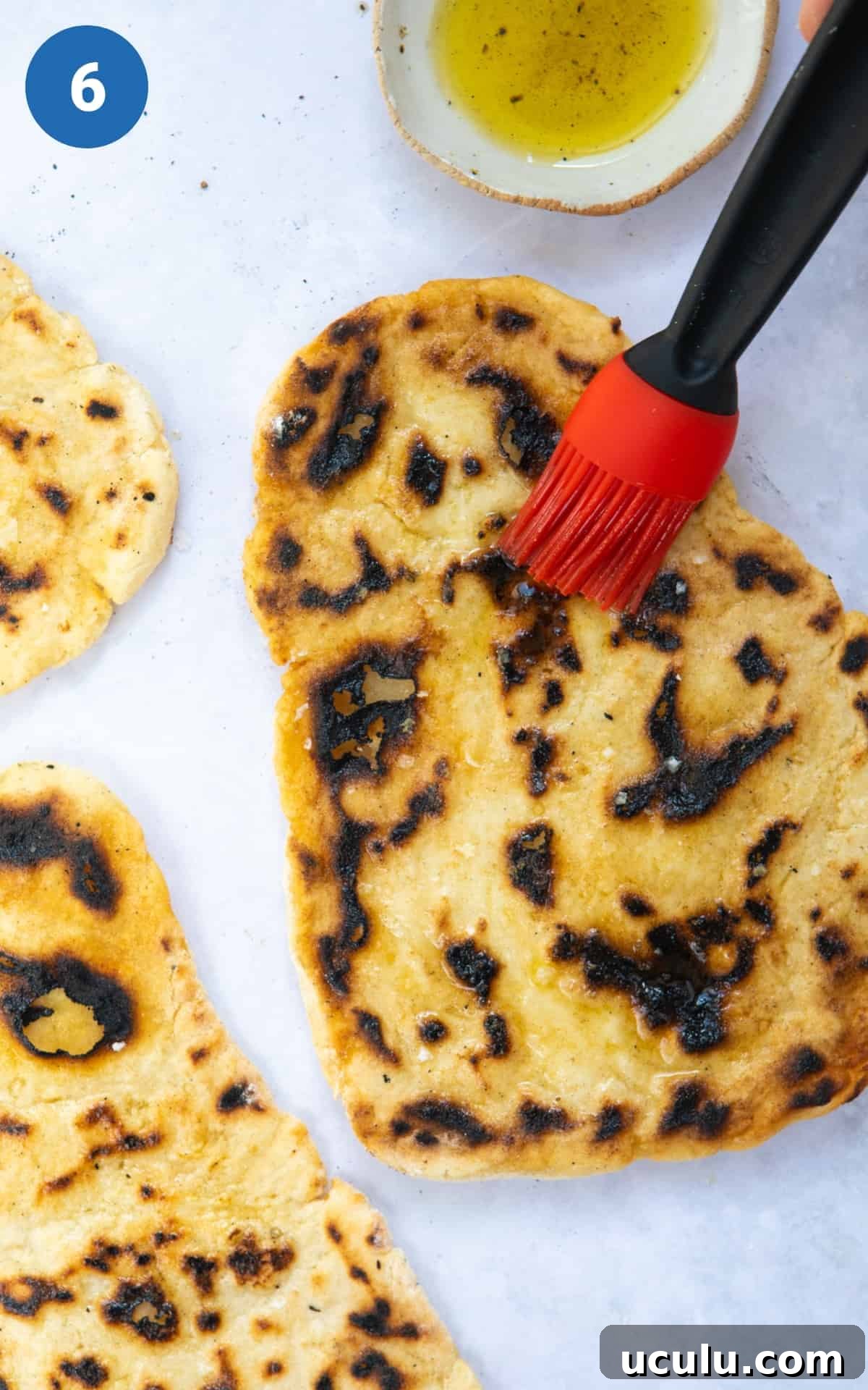 gluten free naan bread on white background being brushed with olive oil.