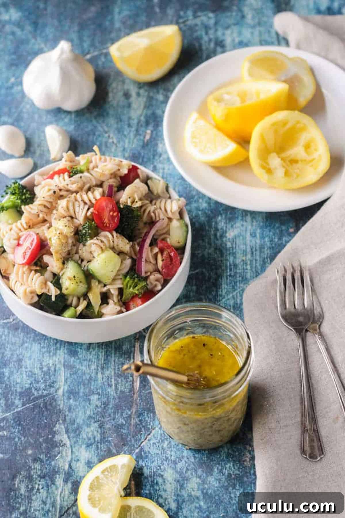 Small bowl of pasta salad next to a jar of vinaigrette and lemon slices.
