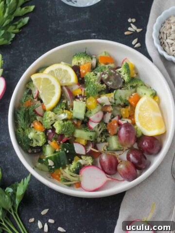 Raw Veggie Chopped Salad in a white bowl garnished with two lemon wedges.