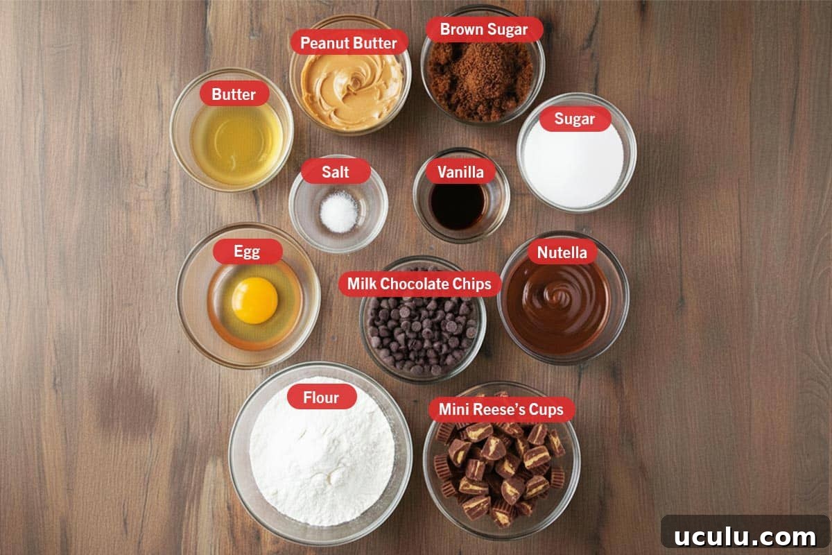 Top shot of ingredients: butter, peanut butter, brown sugar, sugar, egg, salt, vanilla, milk chocolate chips, nutella, flour, and mini Reese's cups.