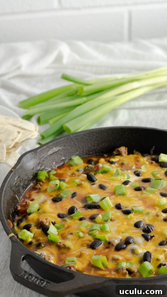 Side view of cast iron skillet and cheesy beef taco skillet with black beans and scallions.