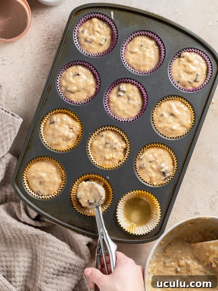 using a cookie scoop to spoon sour cream banana muffin batter into muffin tin