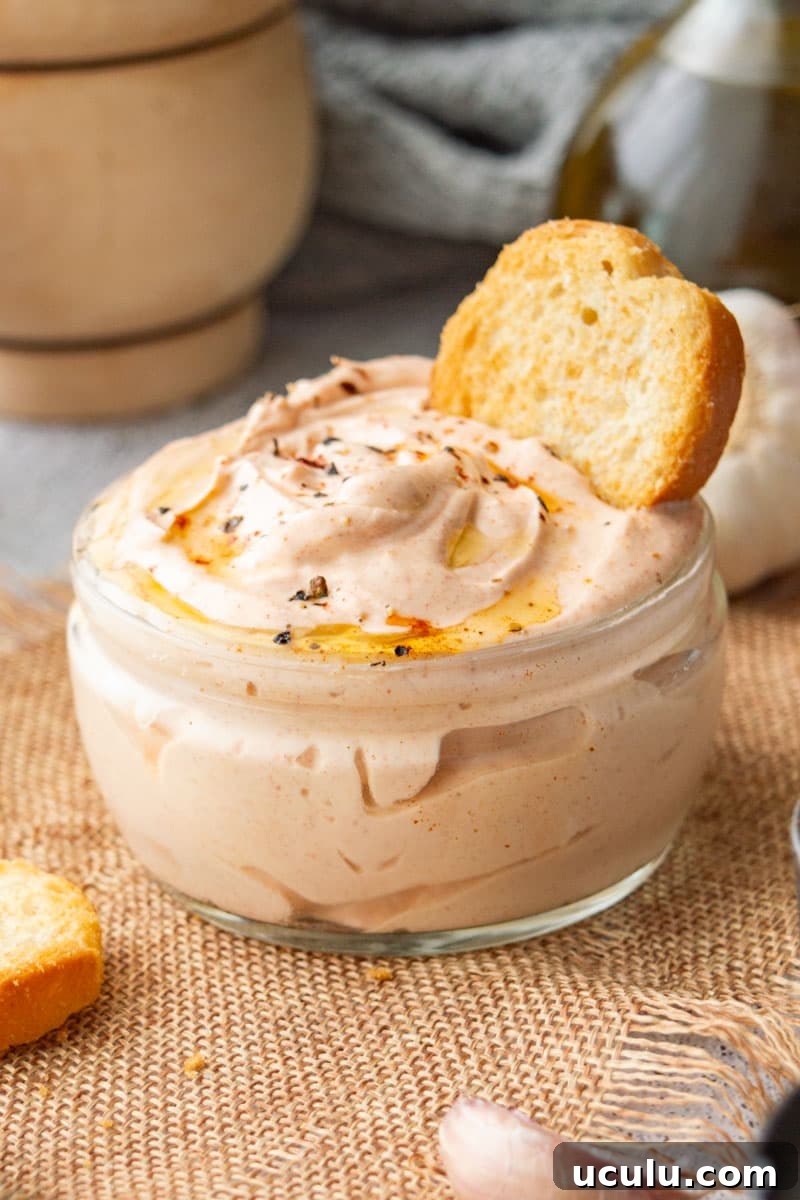 A small glass jar with creamy pink sauce on a beige background.