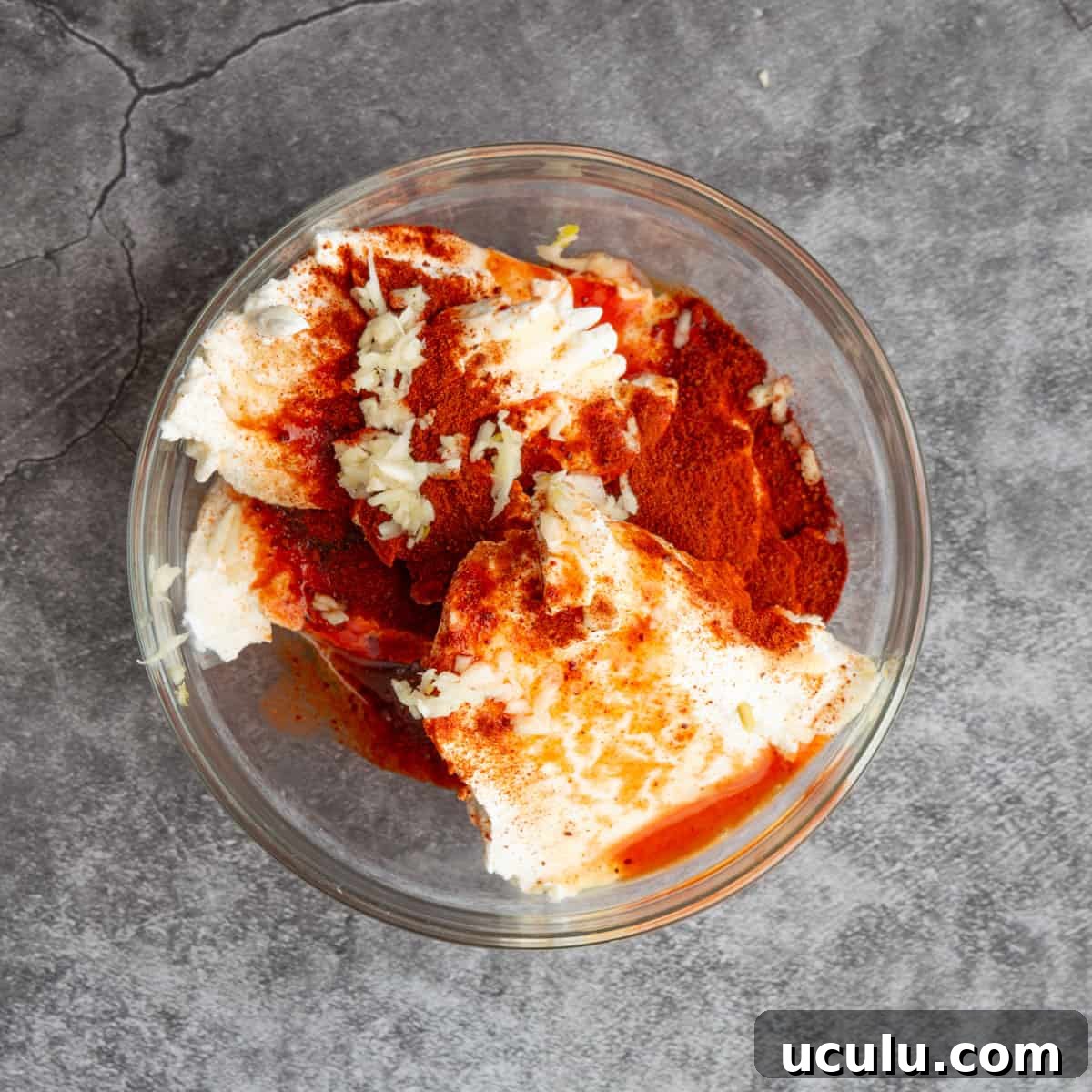 A glass bowl with thick white creamy liquid, and dark red powder.