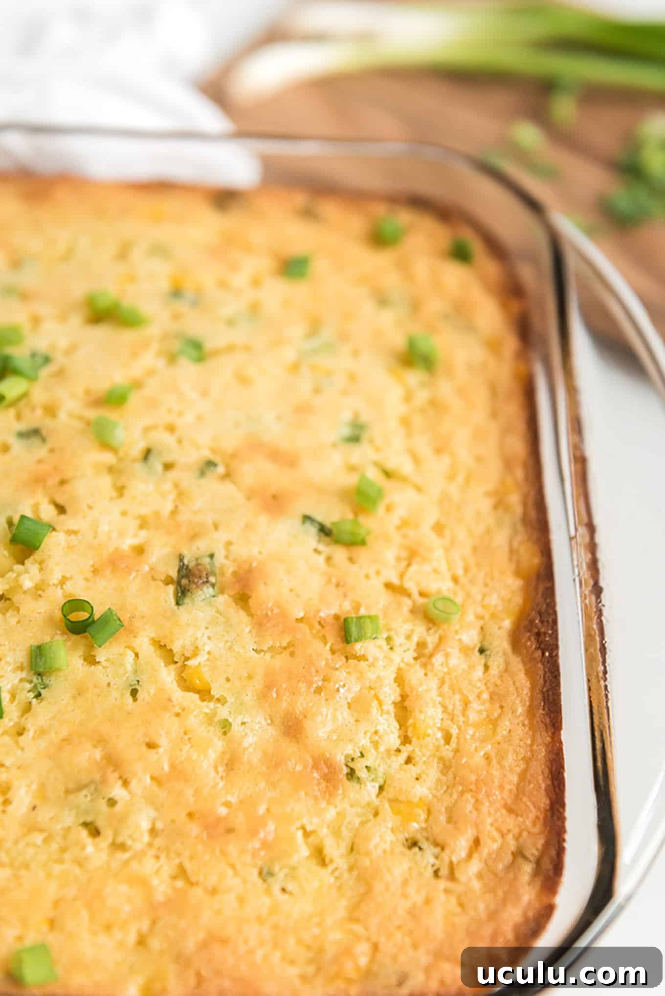 A dish of Jiffy corn casserole sprinkled with green onions on the table.