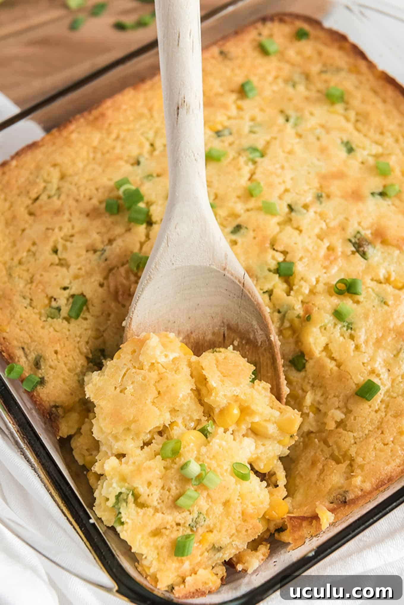 A spoon lifting a serving of Jiffy corn casserole up from the baking dish.