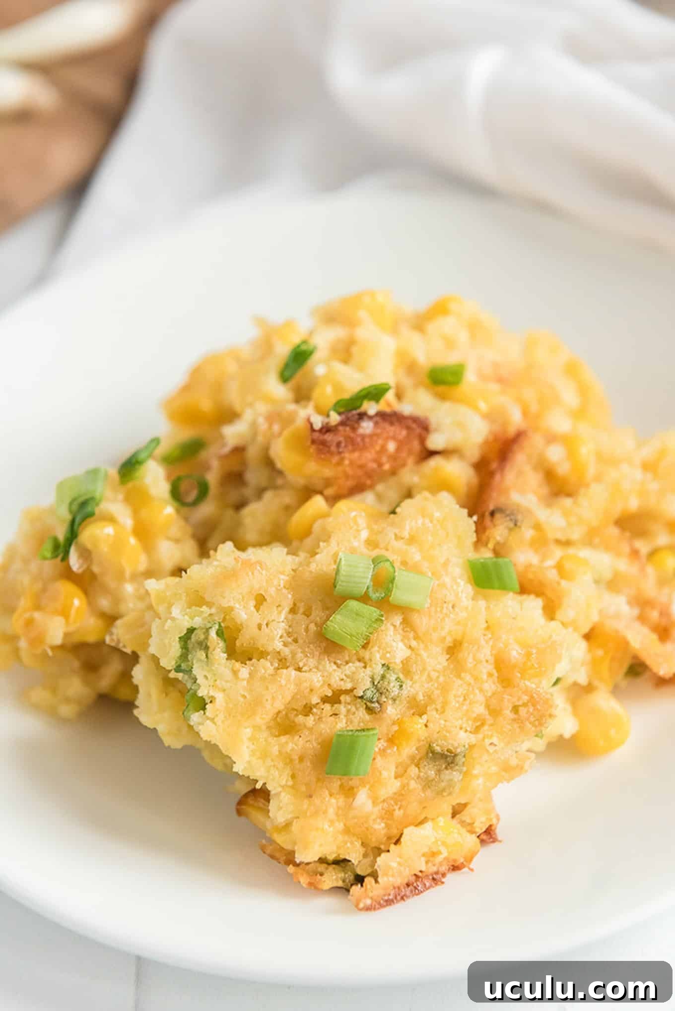 A serving of corn casserole served up on a white plate with green onions on top.