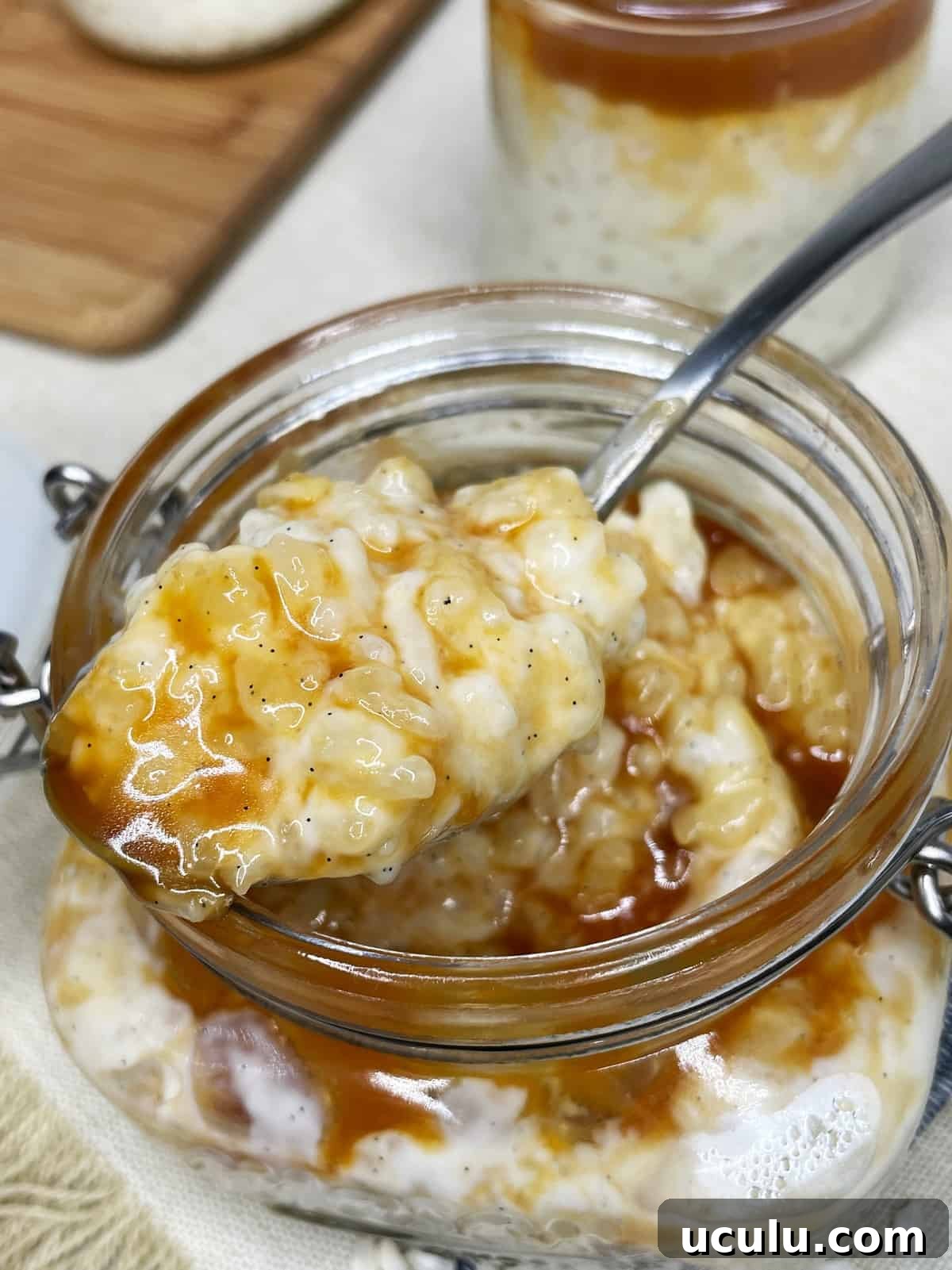 A spoon with French rice pudding mixed with caramel over a glass jar 