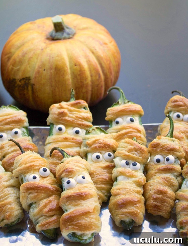 Jalapeño Popper Mummies are a fun and easy Halloween appetizer to make for parties! Simply stuff jalapeño peppers with a cheesy mixture, wrap with strips of crescent dough, and then bake. Don't forget the candy eyes for the finishing touch!