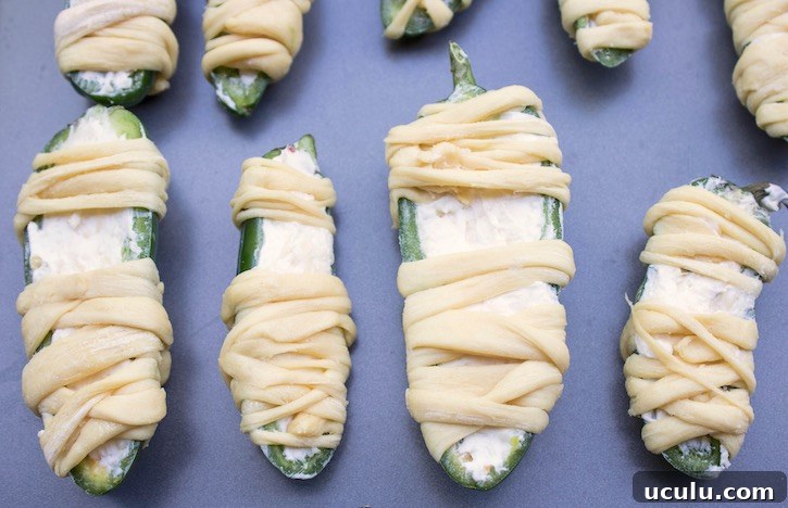 Cream cheese stuffed jalapenos wrapped in refrigerated strips of crescent dough, ready for the oven. 