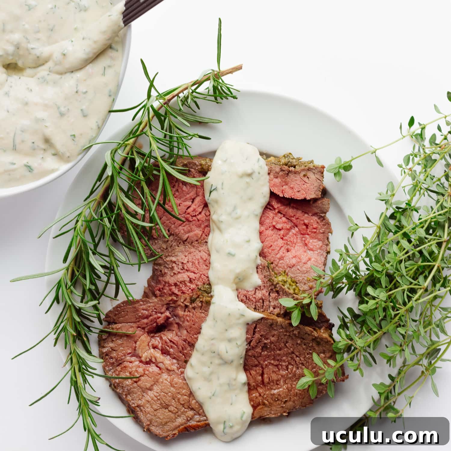 Roast beef slices on a plate with a drizzle of creamy herb sauce down the middle.