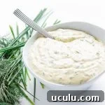White bowl of creamy herb sauce with fresh herbs beside it.