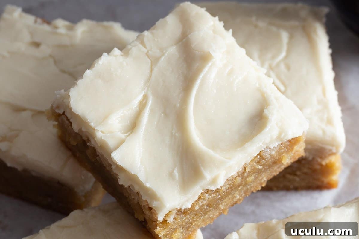 Close up image of frosted blondie brownies sitting on piece of parchment paper.