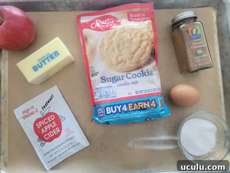 Apple Cider Cookies ingredients, apples, butter, sugar cookie mix, apple cider mix, cinnamon, egg, and sugar on a parchment lined baking sheet