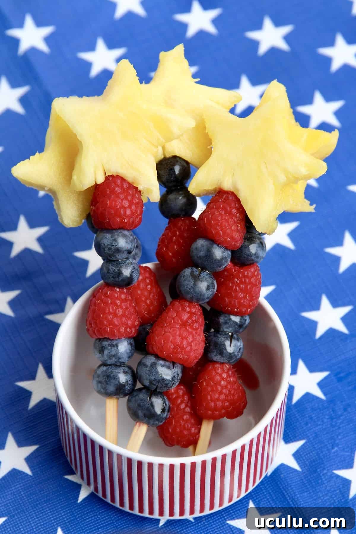 Star shaped pineapple pieces, raspberries and blueberries on a cocktail skewer.