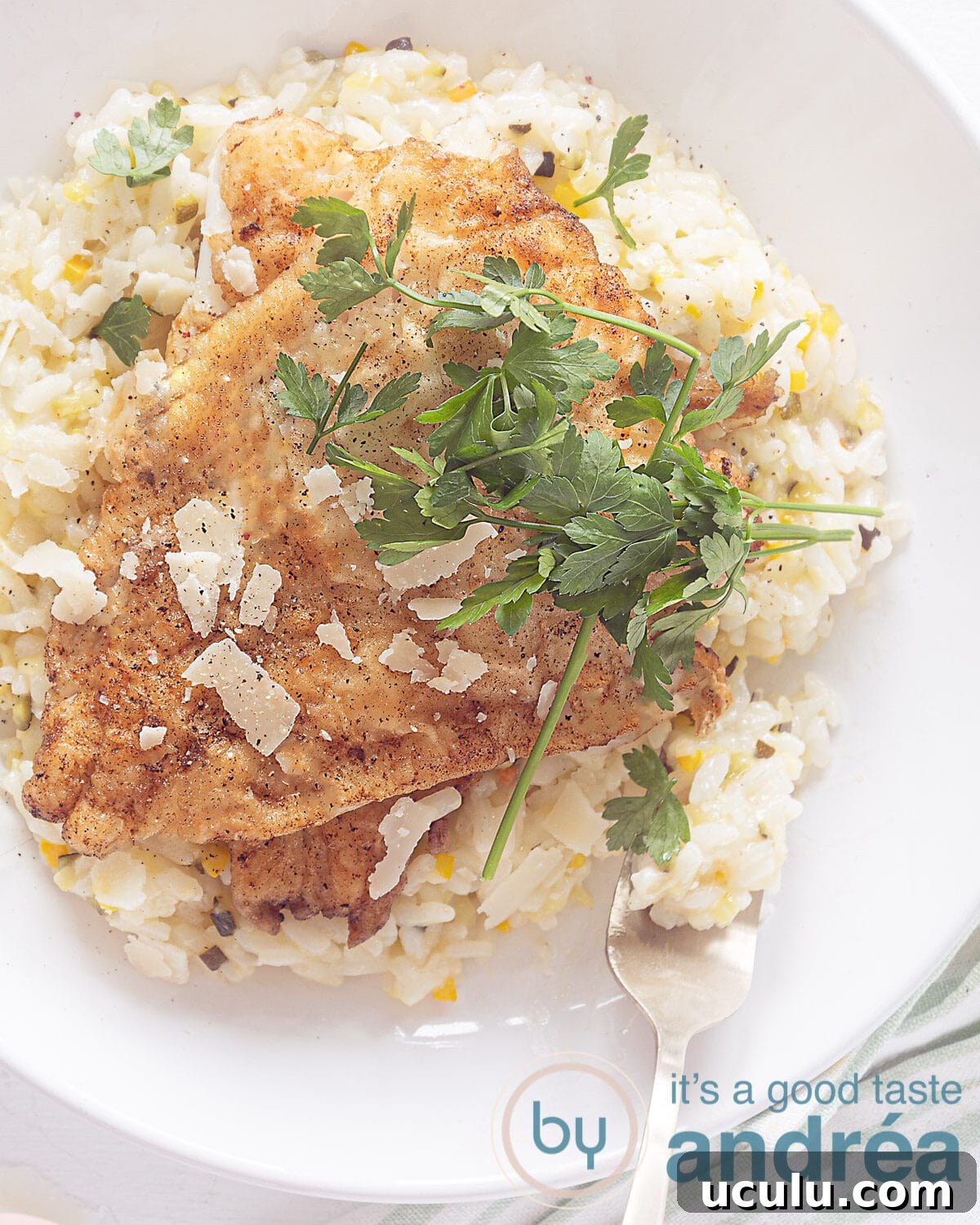 Photo from above of a white plate filled with risotto on which 2 cod fillets lie. Sprinkle parsley on top