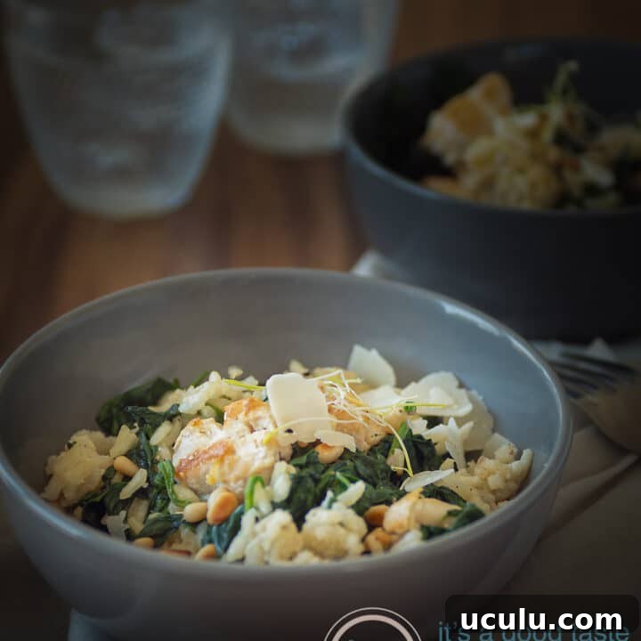 a grey bowl filled with creamy risotto with spinach and chicken. Another bowl in the back as are two glasses