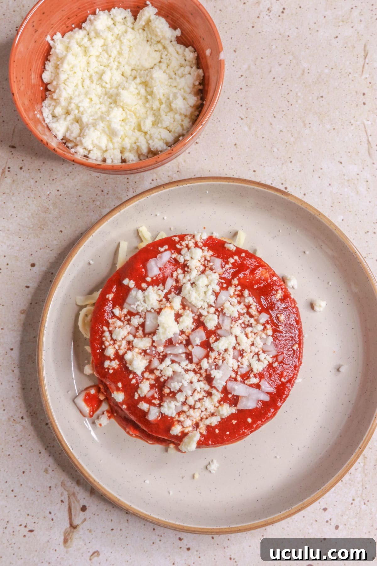 Last layer of stacked enchiladas topped with queso fresco and diced onion