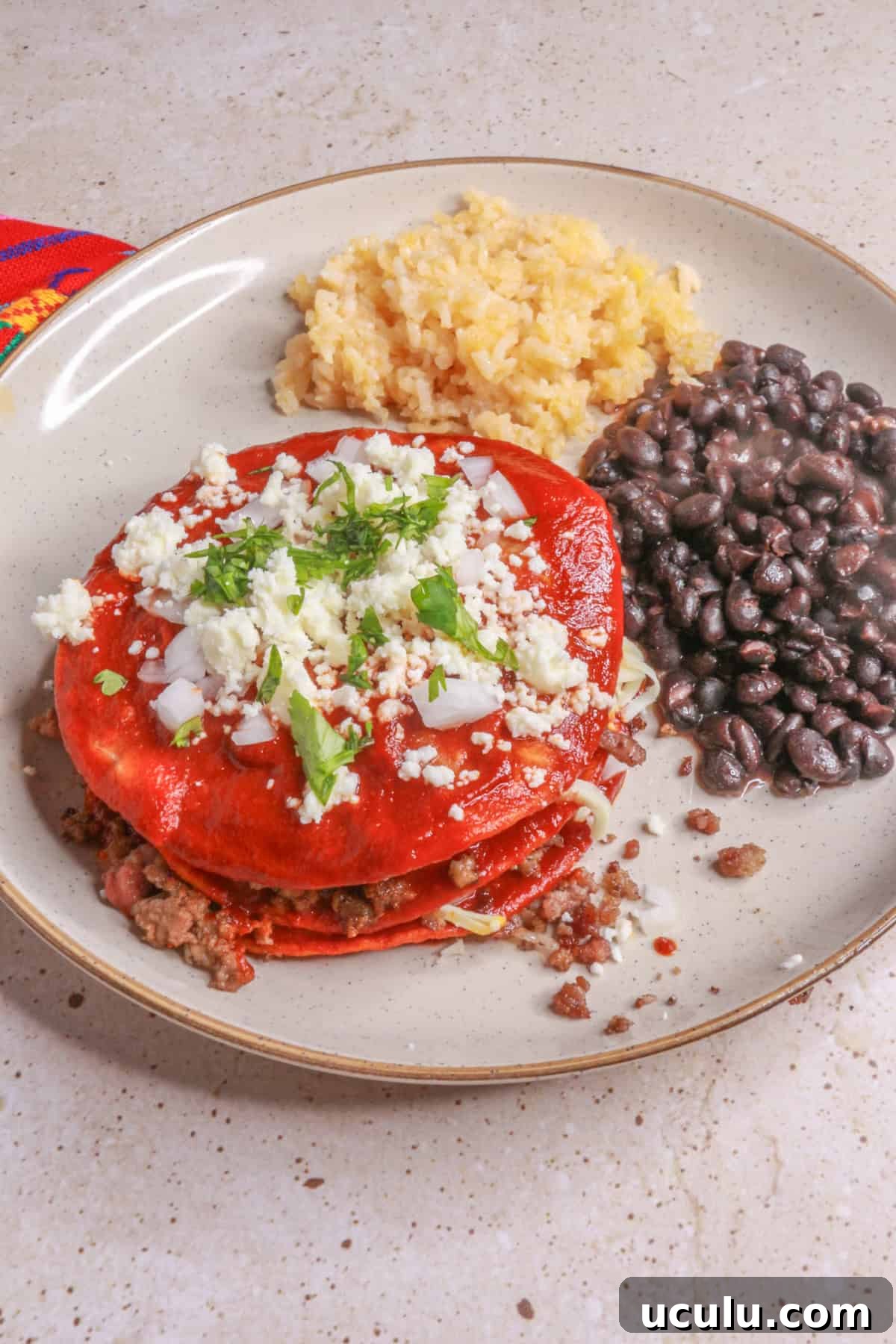 Variation of staked enchiladas with ground beef between layers and served with Mexican red rice and black beans