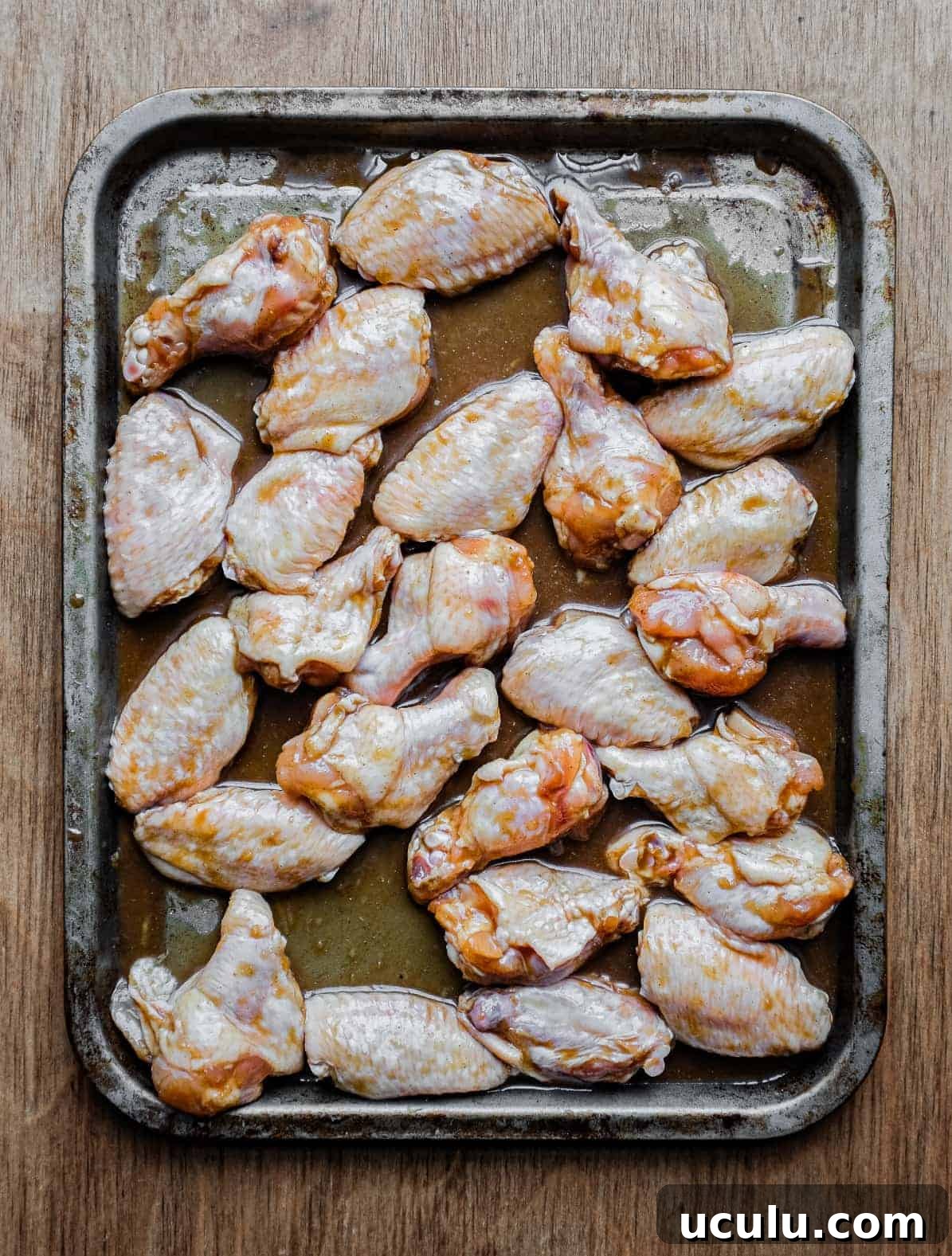 Raw chicken wings on a baking sheet surrounded by a Chinese marinade, just before baking.