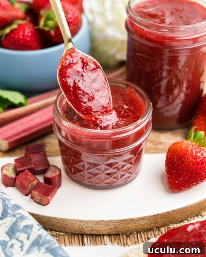 Strawberry and rhubarb preserves in a small jar with a spoon.