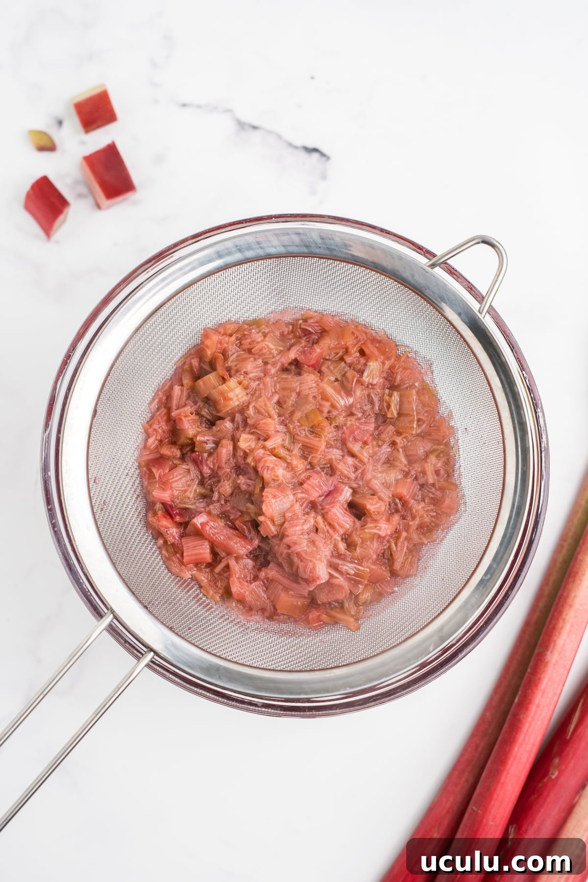 An overhead image of rhubarb being strained from simple syrup.