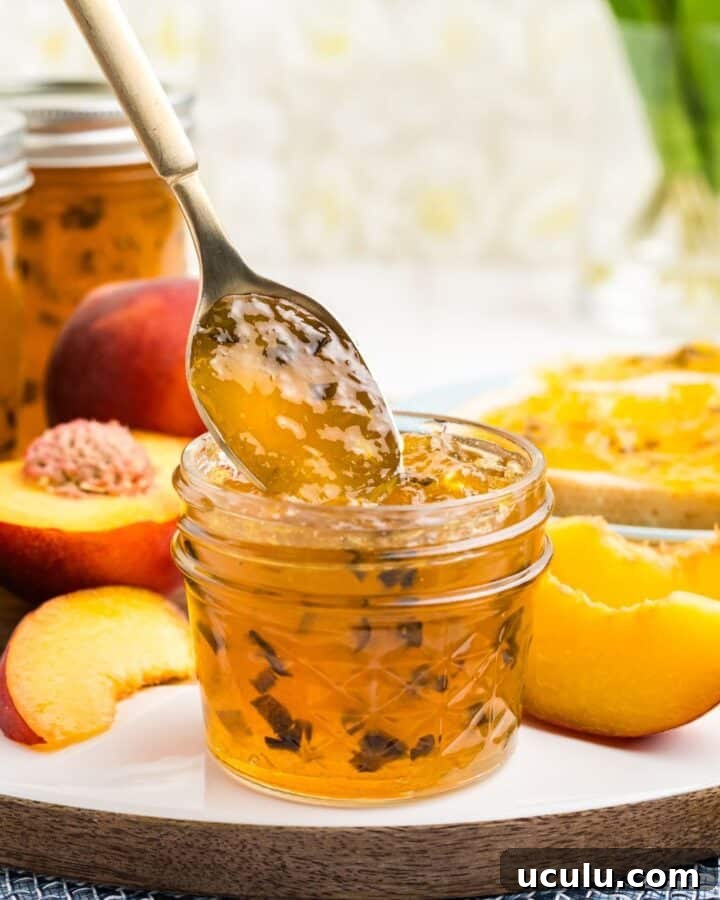 A jar of peach jalapeno jam on a plate with peach slices and a spoon removing a spoonful from the jar.