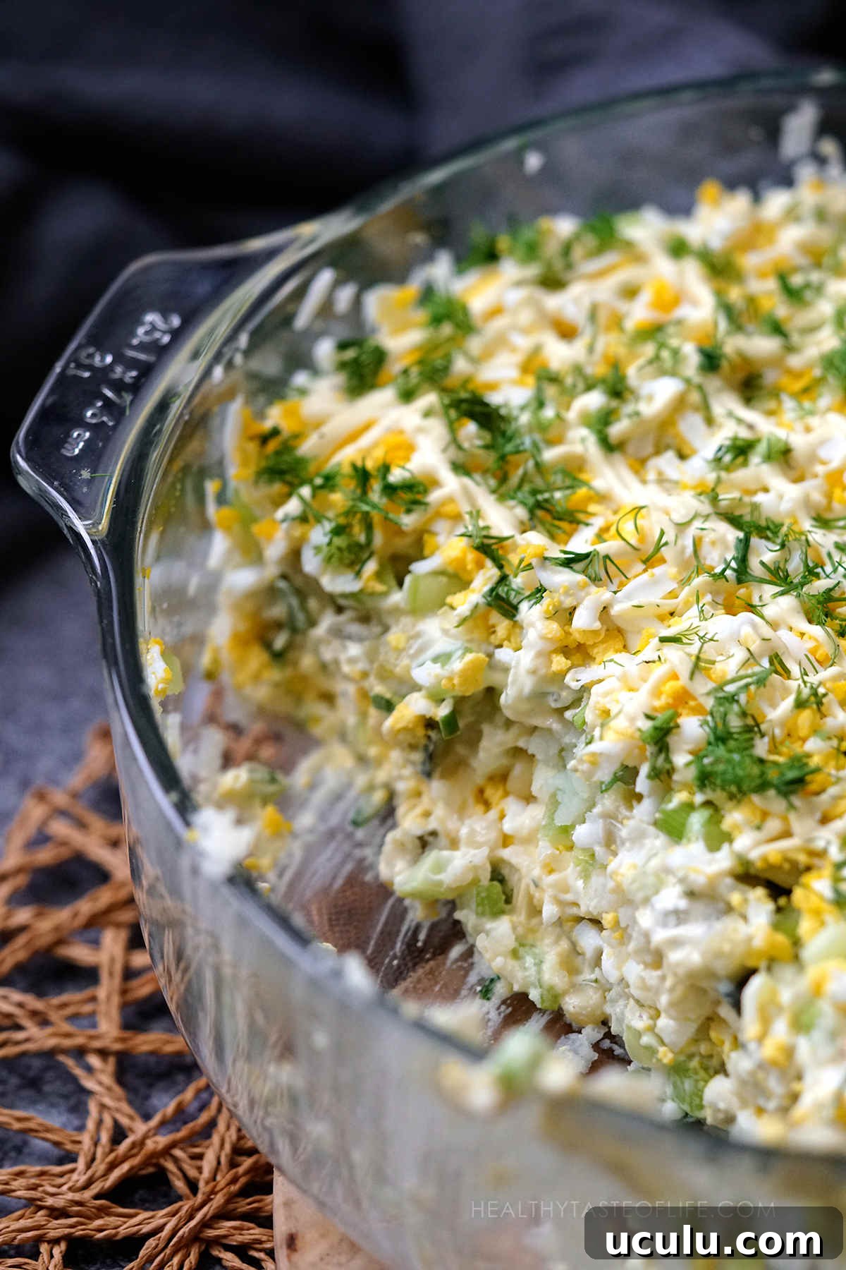 close up shot of potato & egg salad served in a glass dish for Easter, one partion removed showing inside layers ans structure.
