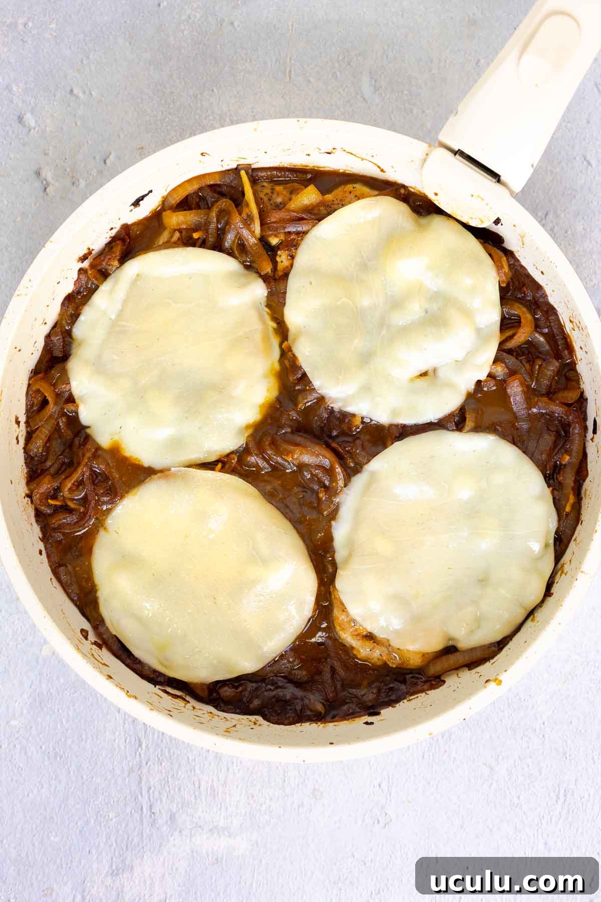 Pork chops in a skillet topped with melted provolone over a bed of caramelized onions.