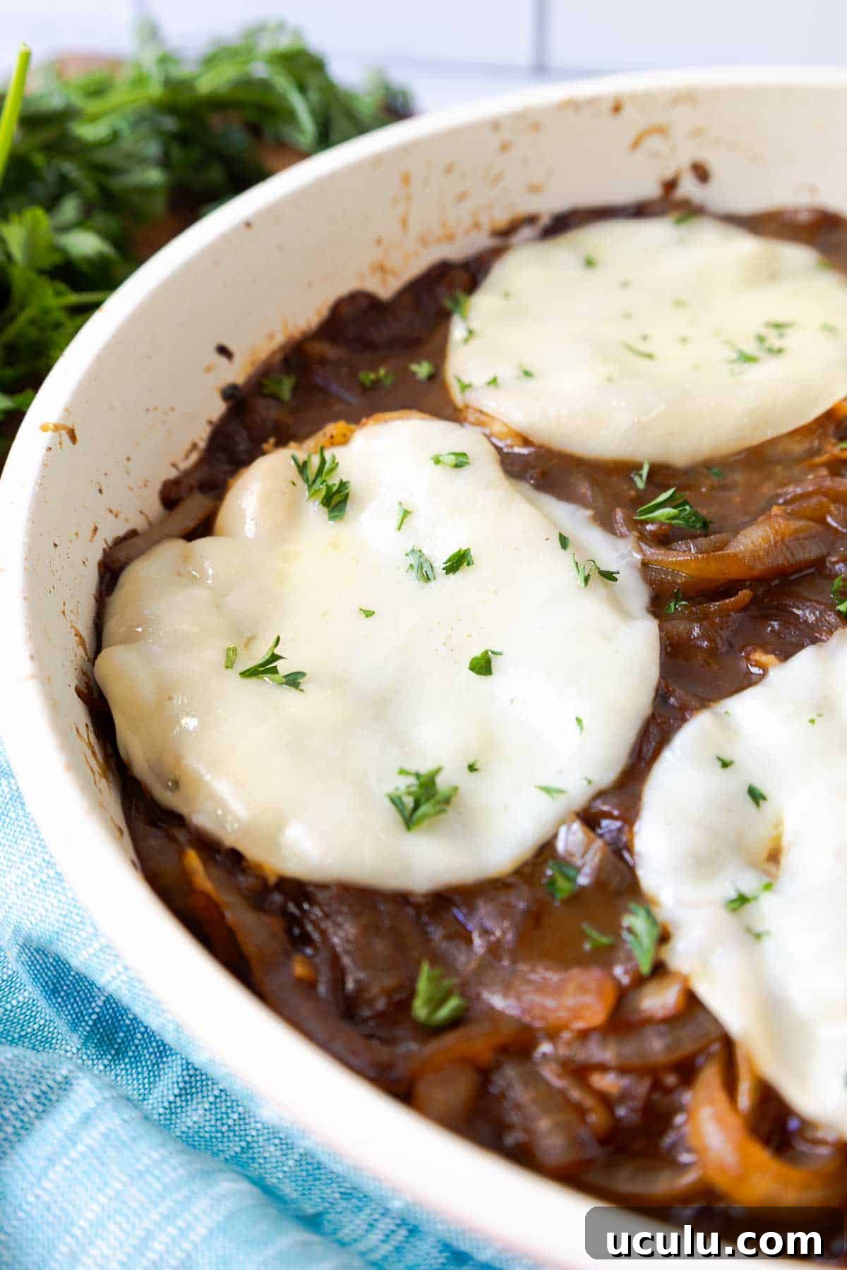 Pork chops in a skillet topped with melted provolone and chopped parsley over caramelized onions.