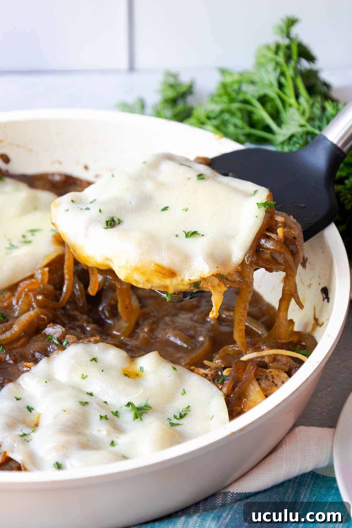 A pork chop being lifted from a skillet with a spatula, topped with melted provolone and onions.