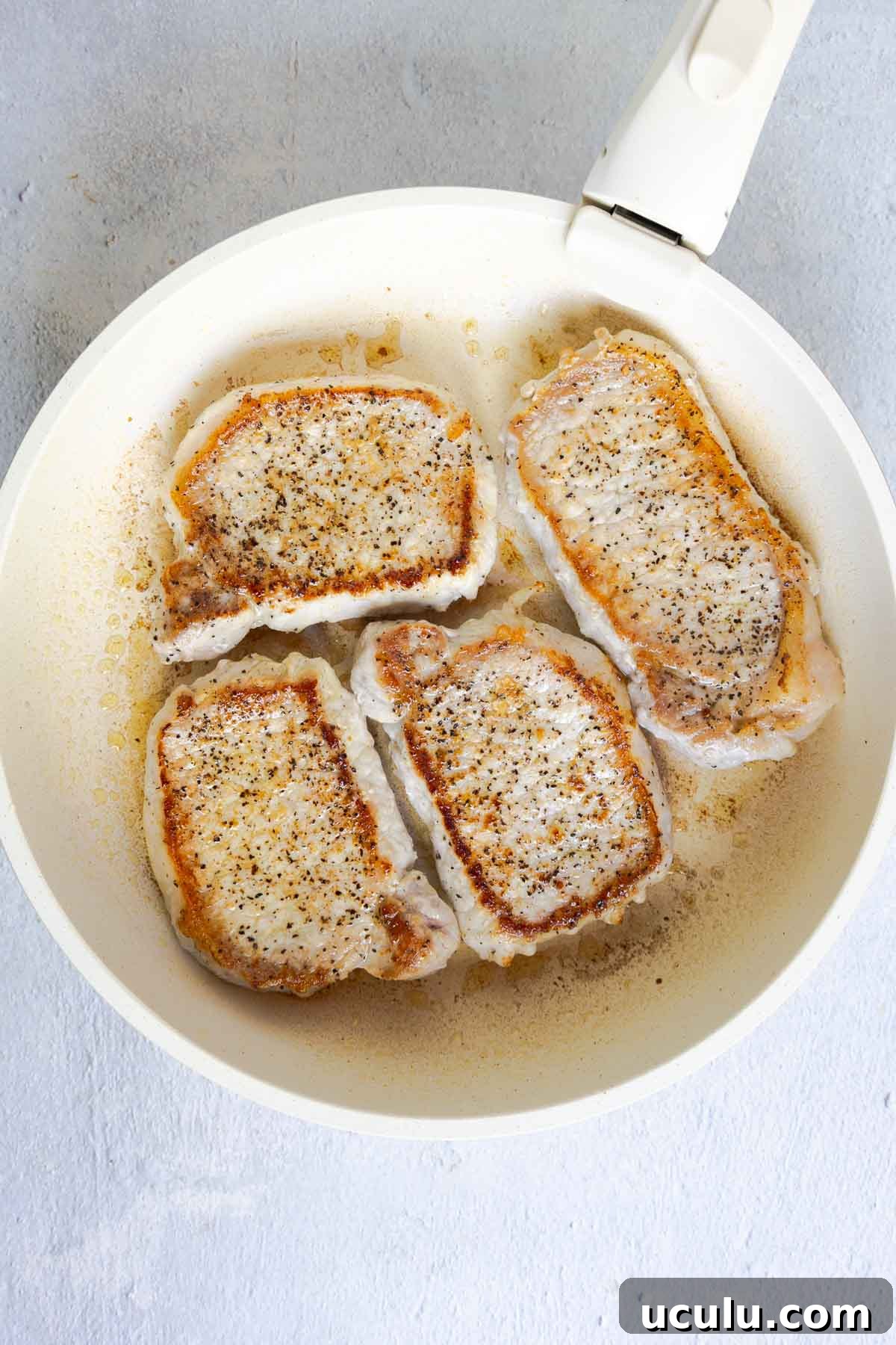 Four pork chops searing in a skillet until golden.