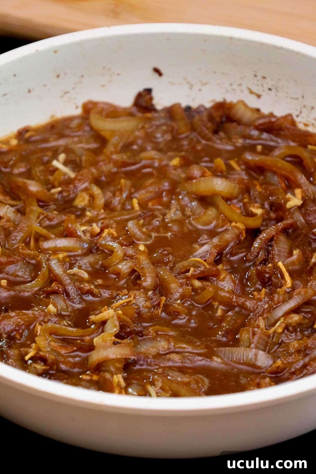 Caramelized onions simmering in broth in a white skillet.