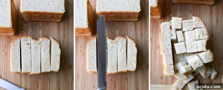 Piles of bread slices on a cutting board being cut into cubes with a bread knife