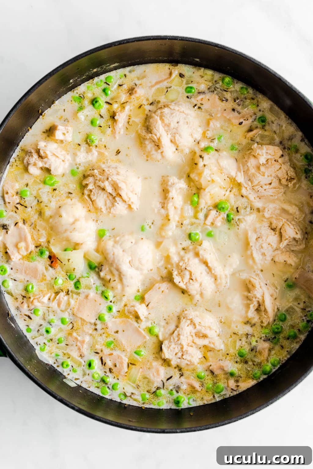 raw dumplings cooking in a large black pot filled with a creamy chicken soup.