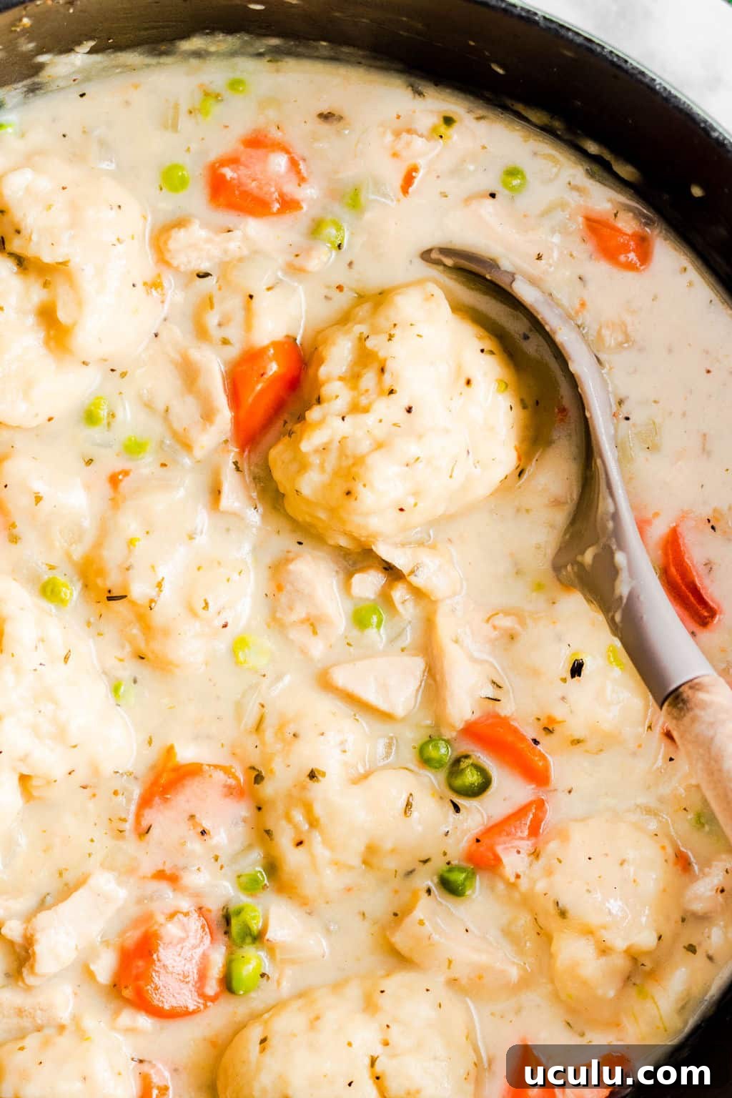 large spoon scooping a dumpling from a large black pot filled with vegan chicken soup and dumplings.