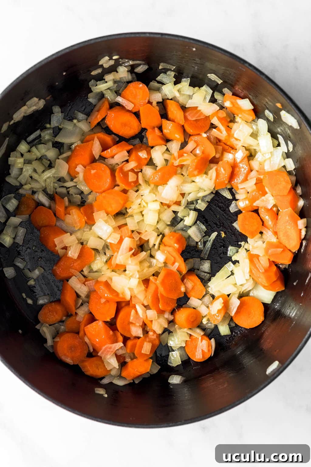 sautéing carrots and onions together in a large black pot.