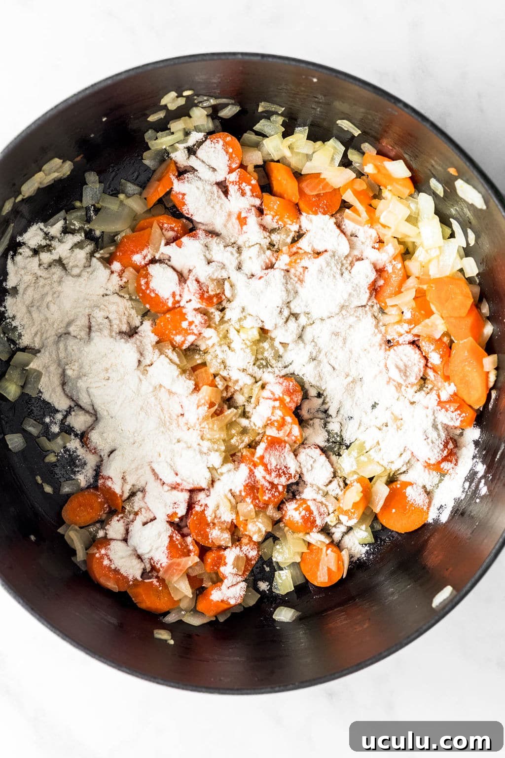 sauteed carrots and onions in a large black pot covered in flour.