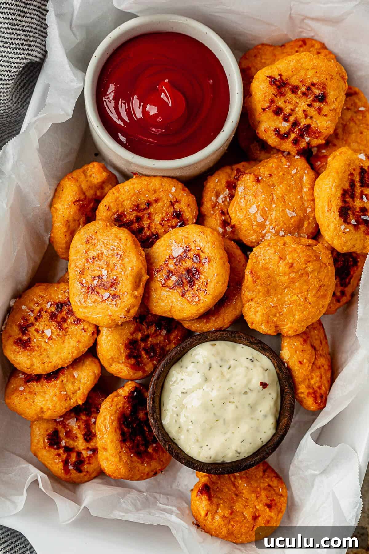 healthy chicken nuggets cooked golden brown in a parchment lined tray with ketchup and ranch