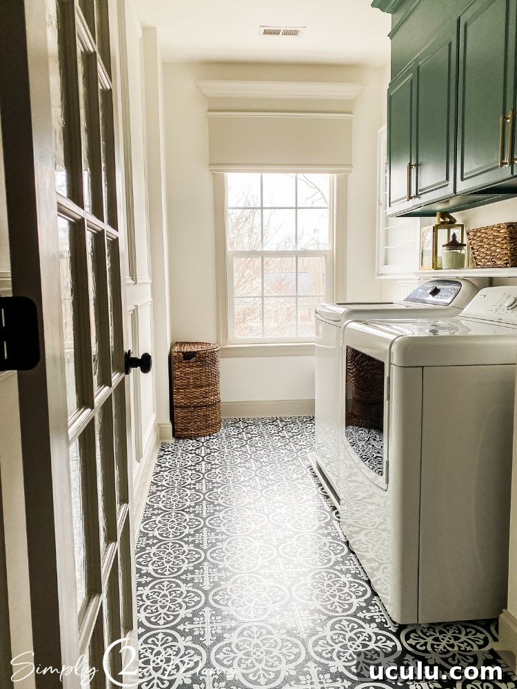 A laundry room with black and white patterned flooring, green cabinets, and wicker accessories/decorations