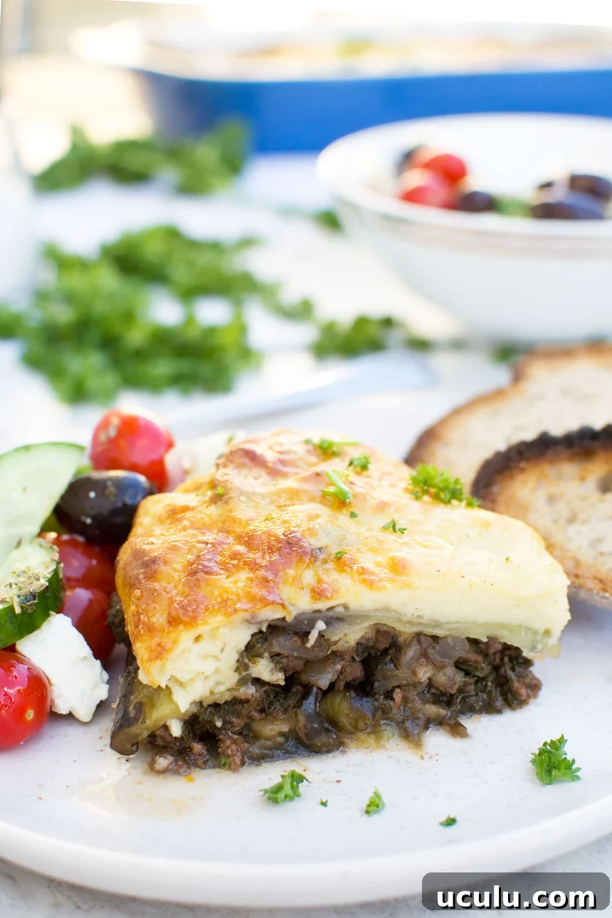 A piece of easy moussaka on a white plate with bread and Greek salad 