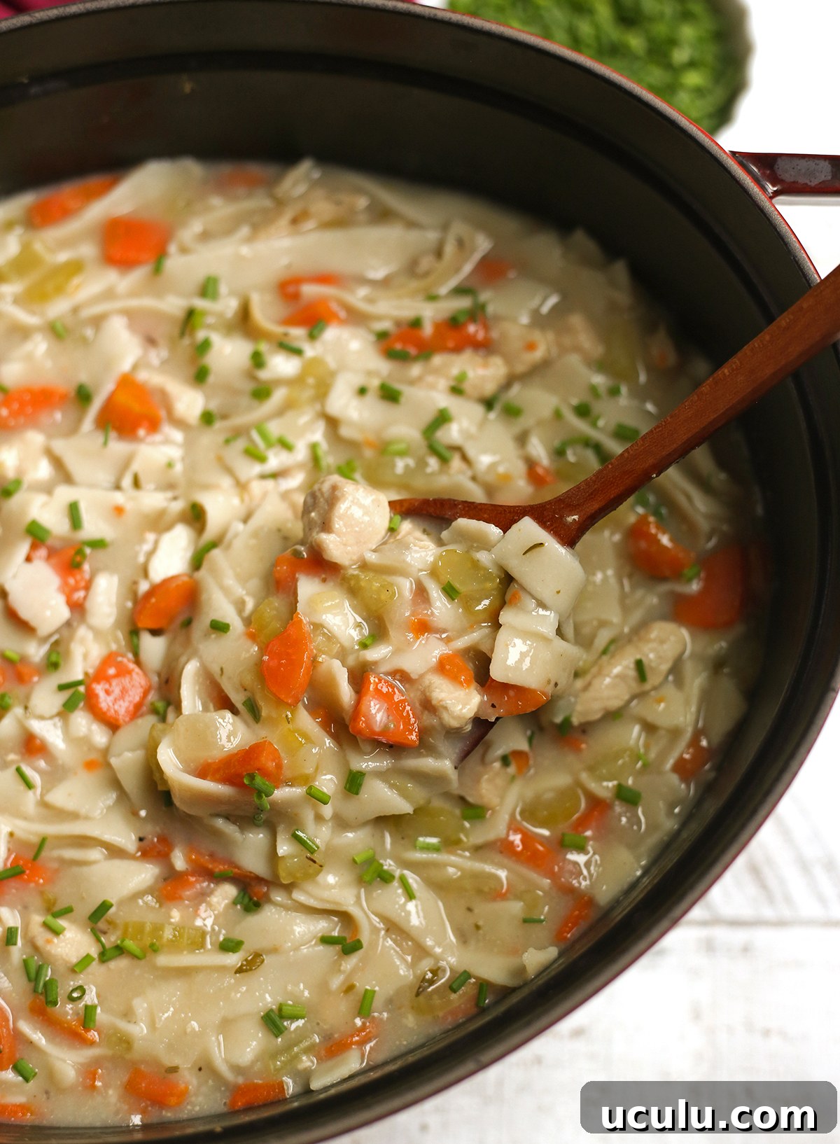 A pot of chicken noodle soup with a serving spoon in it scooping up a serving.