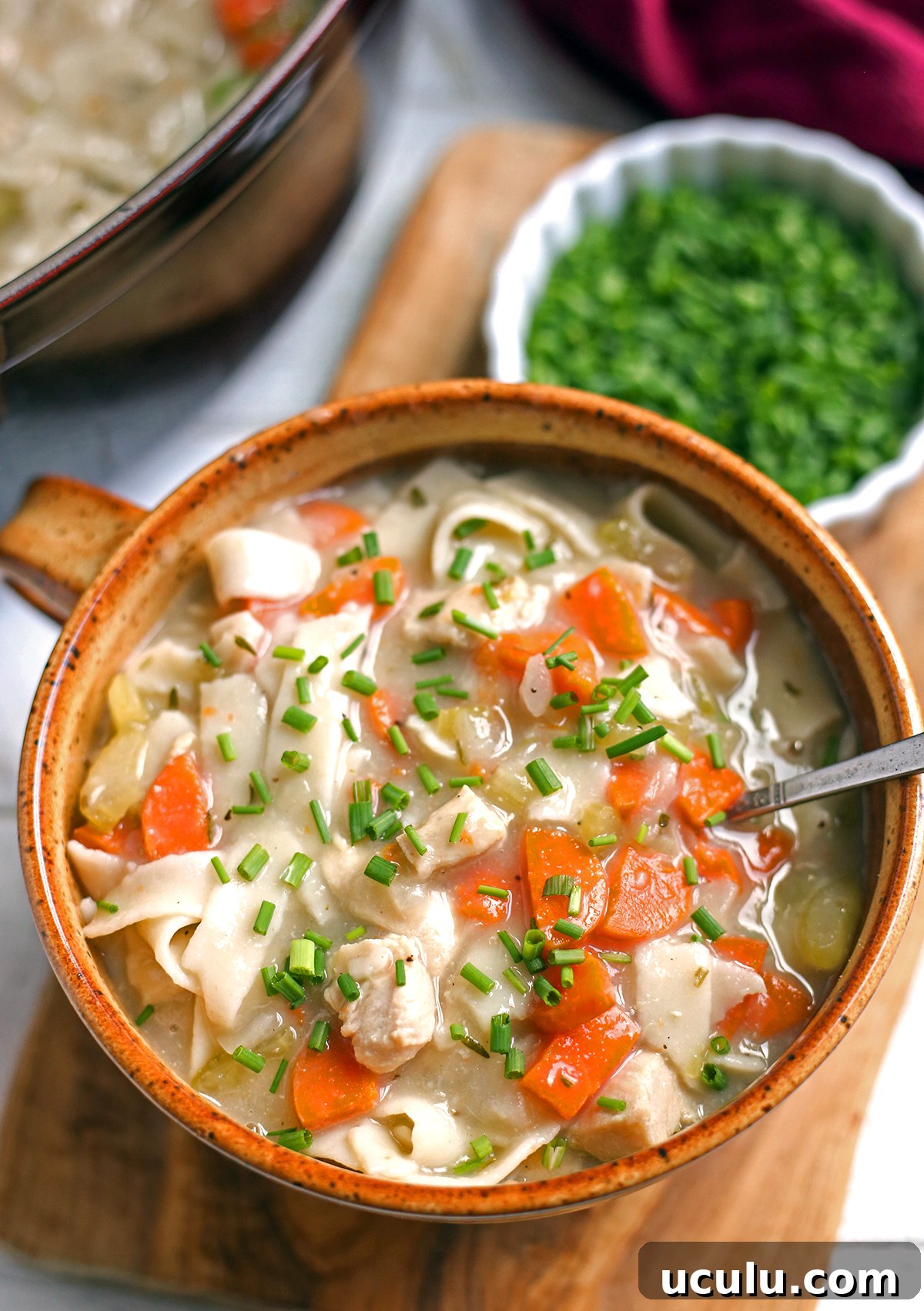Chicken noodle soup in a bowl with a spoon on the side.