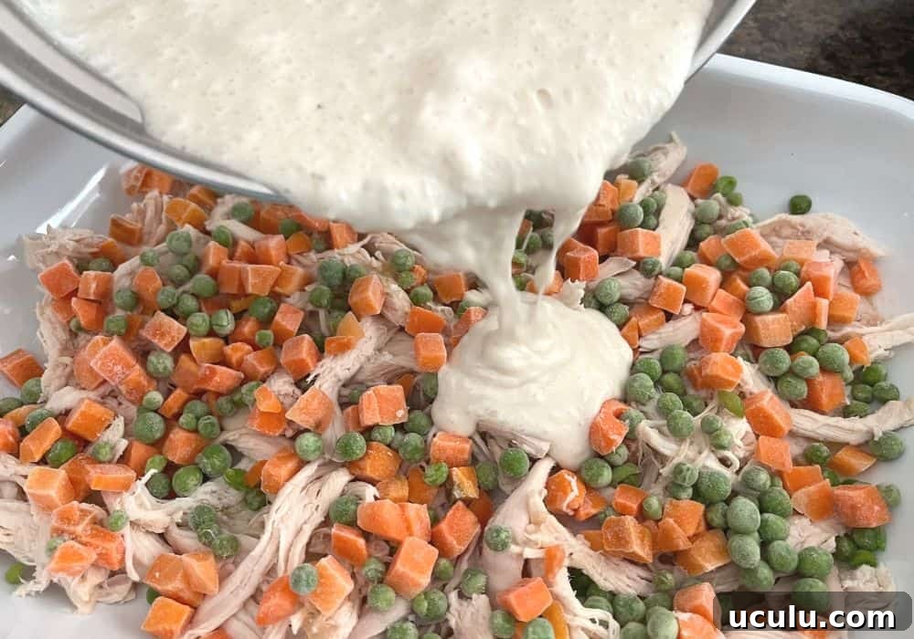 biscuit batter being poured over the chicken and veggies in a baking dish.