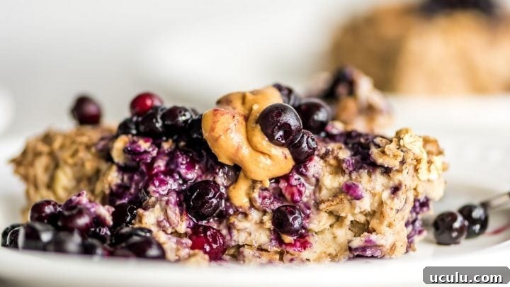 A slice of baked banana oatmeal topped with berries and peanut butter on a plate.
